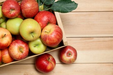 Fresh apples in crate and green leaves on wooden table, top view. Space for text