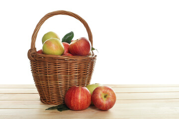 Fresh apples in wicker basket and green leaves on wooden table against white background