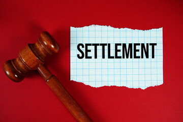 Settlement text written on rip paper with wooden judgment gavel on red background