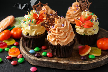 Delicious cupcakes with bat topper, sprinkles, chocolate web and colorful candies on dark table, closeup. Halloween celebration