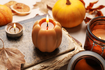 Different burning candles, book and autumn decor on light table, closeup