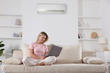 Woman with laptop under air conditioner on sofa at home