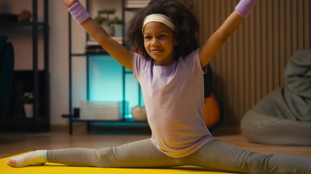 Smiling African American girl performing split at home, children gymnastics