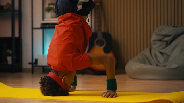African American boy doing headstand during breakdance, active hobby at home