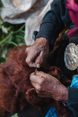 Hands of an elderly woman working wool by hand to turn it into fabric, Tupe, Peru.