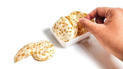 Hand taking Keripik Tempe or Tempeh Chips in white bowl. Isolated on white background with copy space. Traditional Indonesian food are made from soybeans mixed with rice flour then sliced ​​thinly.