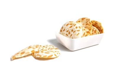 Keripik Tempe or Tempeh Chips in white bowl. Isolated on white background with copy space. Traditional Indonesian food are made from soybeans mixed with rice flour then sliced ​​thinly.