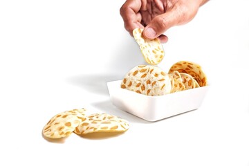 Hand taking Keripik Tempe or Tempeh Chips in white bowl. Isolated on white background with copy space. Traditional Indonesian food are made from soybeans mixed with rice flour then sliced ​​thinly.