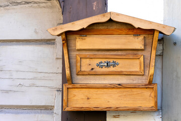 old handmade wooden mailbox with vintage lock on house wall in sunlight
