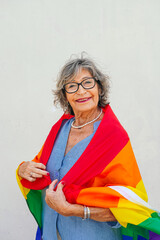 Elderly woman wrapping rainbow flag around shoulders smiling