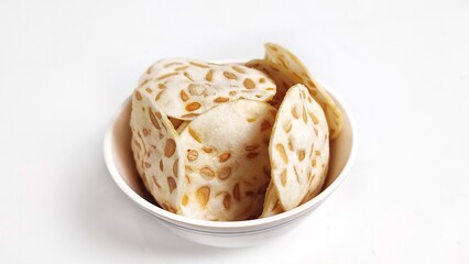 Keripik Tempe or Tempeh Chips in white bowl. Isolated on white background with copy space. Traditional Indonesian food are made from soybeans mixed with rice flour then sliced ​​thinly.
