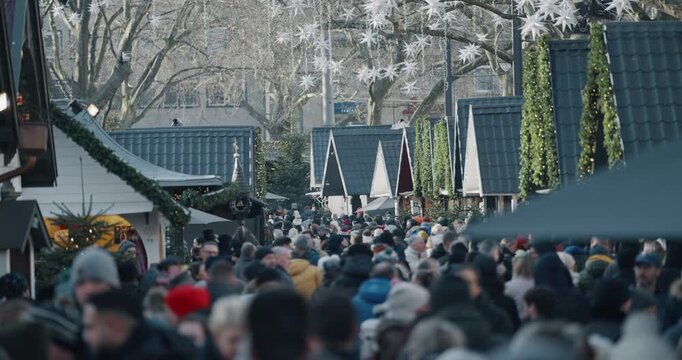 People visiting the Christmas market in Cologne at Neumarkt town square, with many of them wearing hats and coats, slow motion.