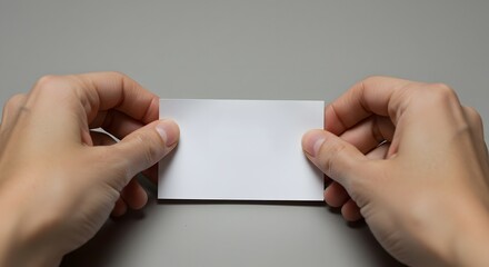 Hands holding a blank white card centered on a gray surface ready for text or graphic design work