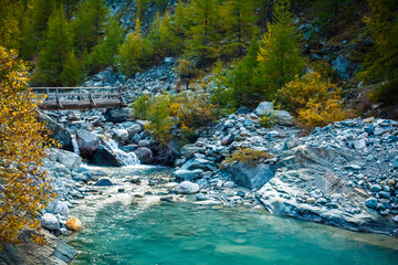 A wooden bridge across an azure mountain river in an autumn forest