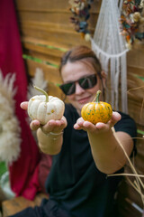  smiling woman holding two small white baby boo and spotted munchkin pumpkins in an outdoor rustic fall display and looking at the camera, concept of seasonal marketing, diy craft, harvest festival