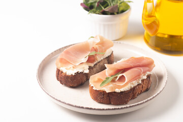 Two bruschettas with prosciutto, ricotta cheese and rucola on ciabatta bread. Olive and spices  decorated.