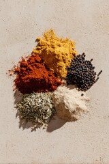 Flat lay image of six spice piles including paprika, turmeric, peppercorns, white powder, fennel seeds, and a spice blend on a warm textured beige background