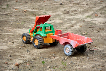 A close-up shot of a brightly colored, plastic toy truck and trailer on a sandy surface, evoking childhood memories of imaginative play in the dirt and sun, and days outdoors.