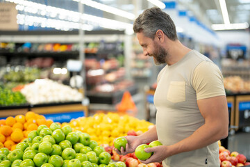 Man shops for fresh apples at a market. Customer chooses organic apples in a grocery store. A male buyer examines raw apples in the produce section of a supermarket. Healthy fruits at grocery store.