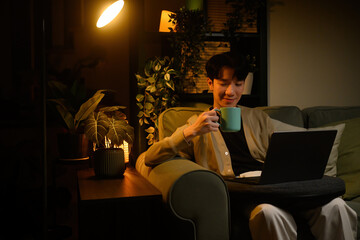 Calm home workspace scene of a man using a laptop at night while sipping coffee in cozy lighting