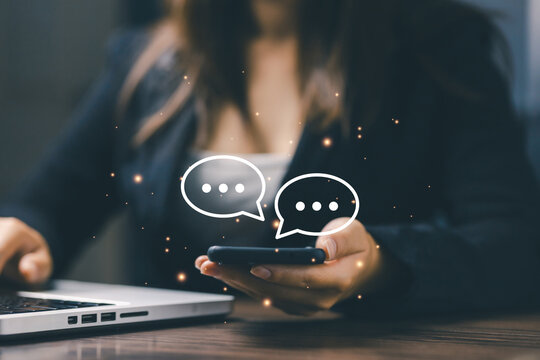 A businesswoman holding a smartphone with chat message icons floating in front, representing online communication, customer service, instant messaging, and digital marketing interaction.