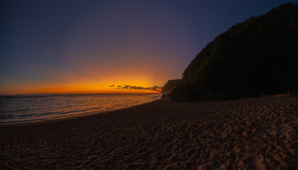 Sunset on Melasti Beach, Bali. Golden light over ocean waves and tropical coastline.