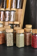 Different spices in glass jars on grey wooden table, closeup