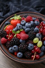 Different ripe berries in bowl on wooden table, closeup