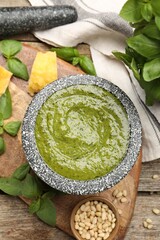 Tasty green pesto in mortar and ingredients on wooden table, flat lay