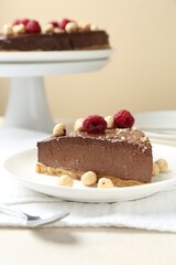 Piece of delicious chocolate cheesecake with nuts and raspberries on beige table, closeup