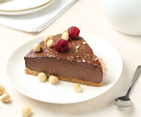Piece of delicious chocolate cheesecake with nuts and raspberries on beige table, closeup