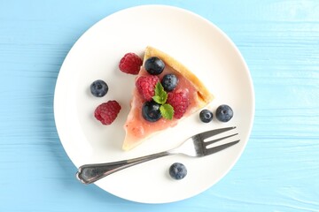 Piece of tasty cheesecake with berries and sauce on light blue wooden table, top view
