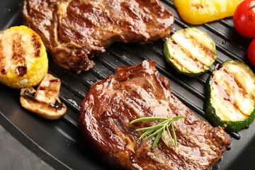 Pan with grilled beef steaks, rosemary, mushroom and vegetables on grey table, above view