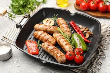 Pan with grilled sausages, vegetables, mushrooms and spices on gray textured table, closeup