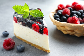 Piece of delicious cheesecake with berries and mint on grey table, closeup