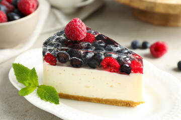 Piece of delicious cheesecake with berries and mint on light grey table, closeup