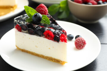 Piece of delicious cheesecake with berries and mint on black wooden table, closeup