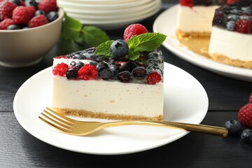 Piece of delicious cheesecake with berries and mint on black wooden table, closeup