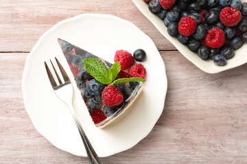 Piece of delicious cheesecake with berries, mint and fork on wooden table, flat lay