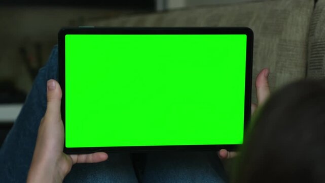 Girl lying on sofa and using digital tech tablet with green screen mock up. Hand scroll web site, swiping. Person hold chroma key device closeup on home background. Online app, education, social media