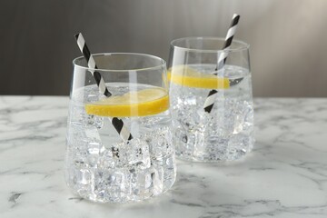 Refreshing water with lemon and ice on white marble table, closeup
