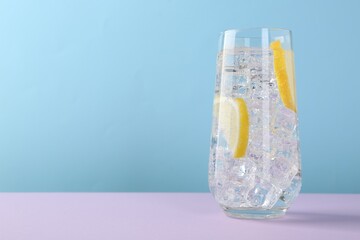 Refreshing water with lemon and ice in glass on violet table against light blue background, closeup. Space for text