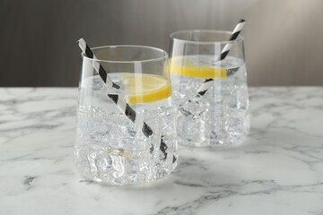Refreshing water with lemon and ice on white marble table, closeup