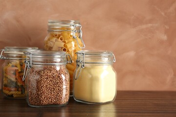 Glass jars with different products on wooden table, closeup. Space for text