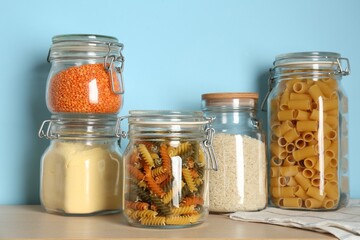 Glass jars with different products on wooden table against light blue background
