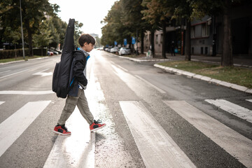 Young boy crossing street with guitar case
