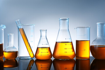 Different glassware with orange liquid on mirror surface against grey background