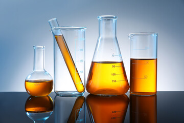 Different glassware with orange liquid on mirror surface against grey background