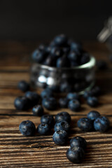 Fresh blueberries scattered on a rustic wooden surface. Still life composition with soft lighting and a blurred background. Concept of healthy eating, organic food, and natural freshness.