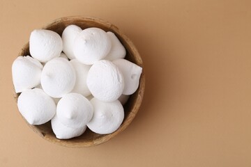 Delicious meringue cookies in bowl on beige background, top view. Space for text